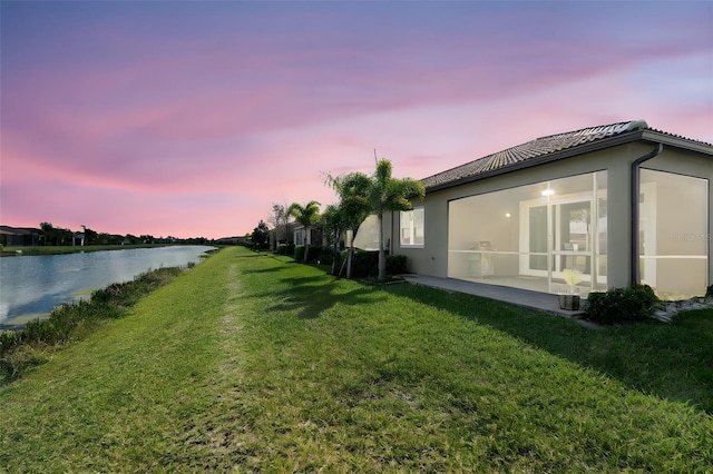 yard at dusk with a sunroom and a water view