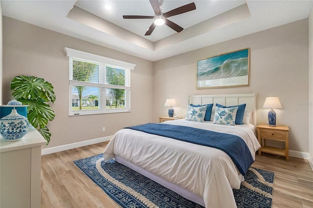 bedroom featuring light wood finished floors, a tray ceiling, a ceiling fan, and baseboards