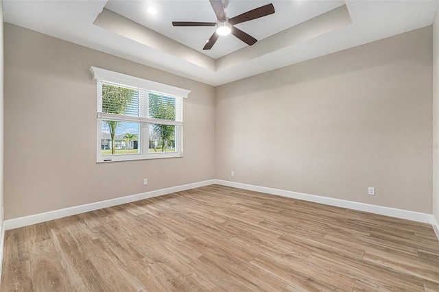 empty room featuring light wood-type flooring, baseboards, a tray ceiling, and ceiling fan