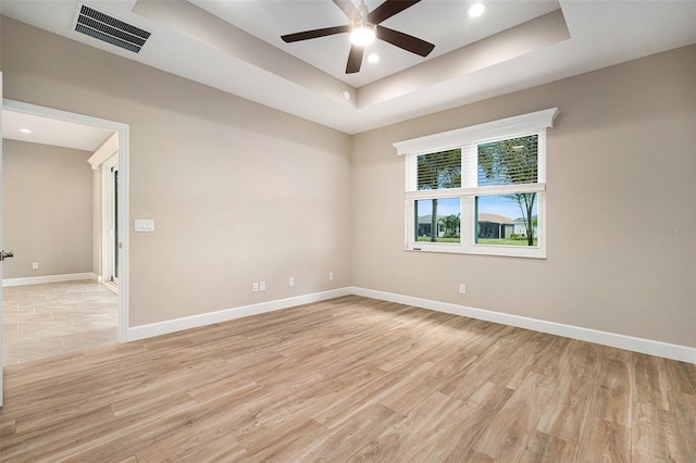 spare room with a tray ceiling, visible vents, ceiling fan, light wood-type flooring, and baseboards