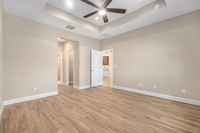 empty room with visible vents, baseboards, a ceiling fan, light wood-style flooring, and a tray ceiling