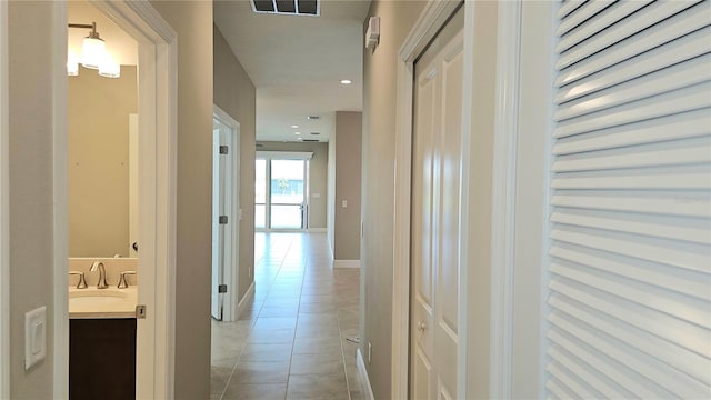 hallway featuring light tile patterned floors, recessed lighting, a sink, visible vents, and baseboards