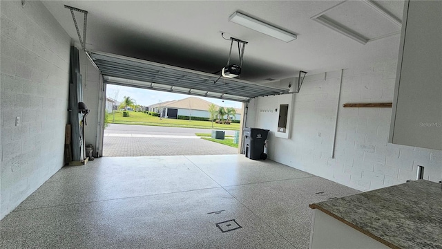 garage featuring concrete block wall, electric panel, and a garage door opener