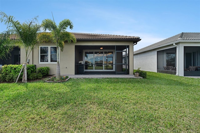 rear view of property featuring a sunroom, a tile roof, a lawn, and stucco siding