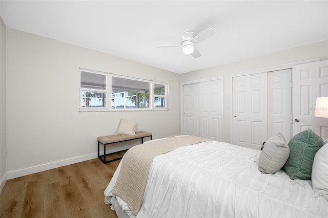 bedroom with ceiling fan, two closets, baseboards, and wood finished floors