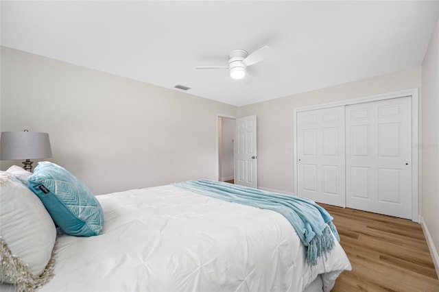 bedroom with a ceiling fan, wood finished floors, visible vents, baseboards, and a closet