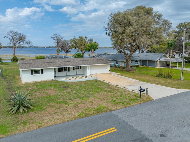 ranch-style house with a front lawn, an attached garage, a water view, and driveway