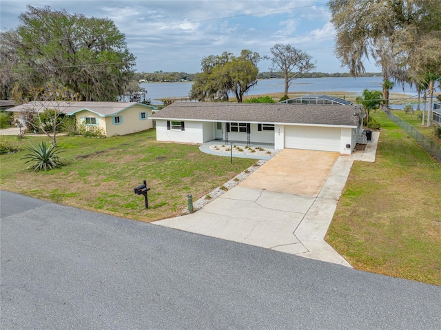 ranch-style house featuring a water view, concrete driveway, a front yard, stucco siding, and an attached garage