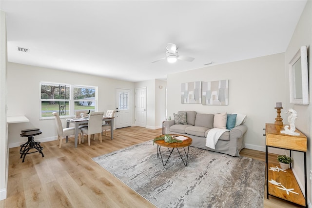 living area featuring visible vents, baseboards, a ceiling fan, and light wood finished floors