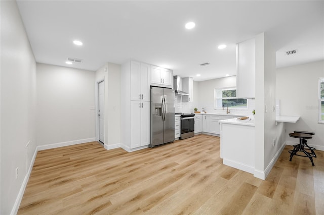 kitchen featuring visible vents, light wood-style flooring, stainless steel appliances, and wall chimney range hood