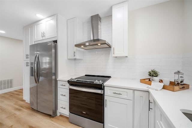 kitchen with visible vents, wall chimney range hood, white cabinetry, stainless steel appliances, and light countertops