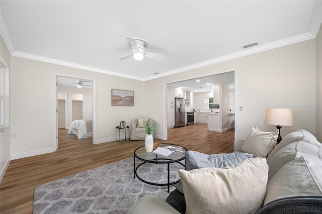 living area with visible vents, baseboards, light wood-style floors, and ornamental molding