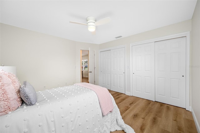 bedroom featuring visible vents, two closets, wood finished floors, baseboards, and ceiling fan