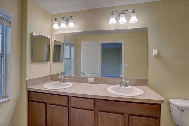 bathroom with double vanity, a sink, and toilet