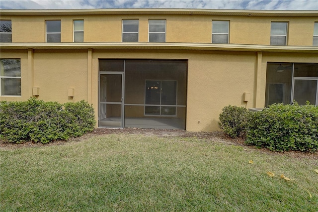 rear view of property with a lawn, a sunroom, and stucco siding