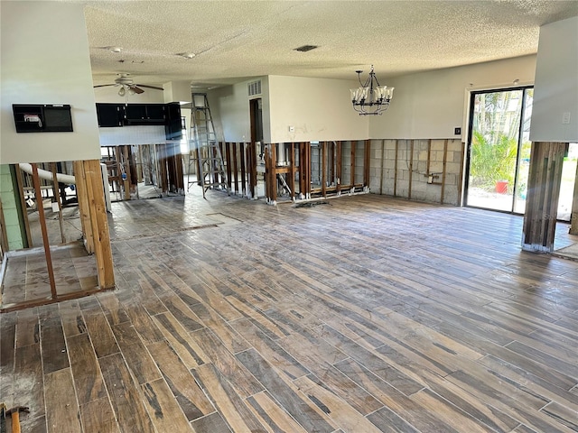 unfurnished living room featuring a textured ceiling, visible vents, wood finished floors, and ceiling fan with notable chandelier