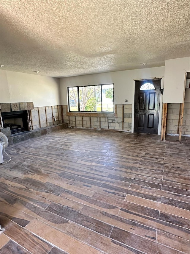 unfurnished living room featuring dark wood-type flooring, a fireplace, and a textured ceiling