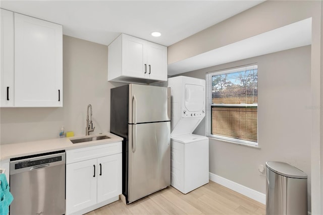 kitchen featuring baseboards, stacked washer and clothes dryer, appliances with stainless steel finishes, light countertops, and a sink