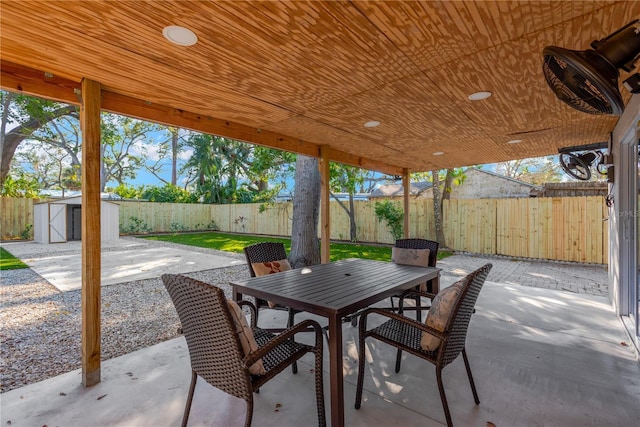 view of patio featuring outdoor dining space, a fenced backyard, an outbuilding, and a storage shed