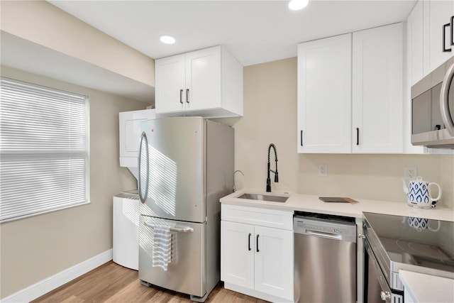 kitchen featuring light wood finished floors, baseboards, stainless steel appliances, white cabinetry, and a sink