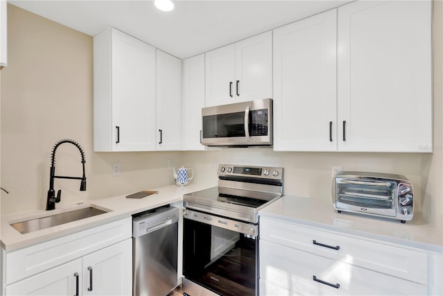 kitchen with light countertops, appliances with stainless steel finishes, a sink, and white cabinets