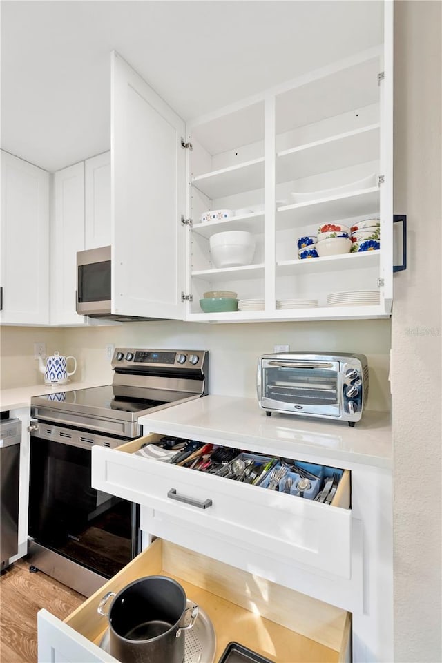 kitchen with a toaster, white cabinetry, light countertops, appliances with stainless steel finishes, and open shelves