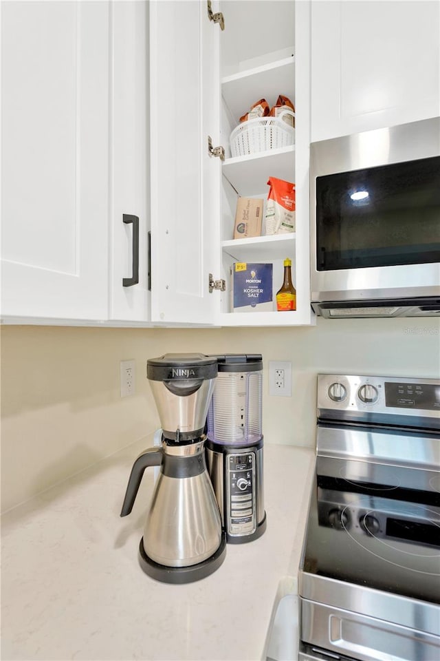 room details featuring open shelves, appliances with stainless steel finishes, light stone counters, and white cabinets