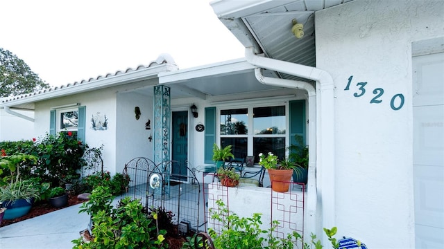 view of exterior entry featuring a garage, covered porch, and stucco siding