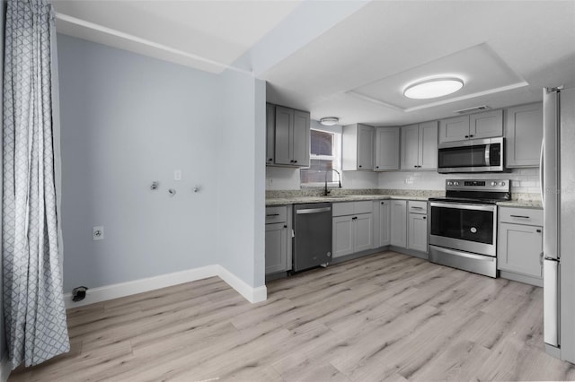 kitchen with gray cabinetry, stainless steel appliances, a sink, baseboards, and light wood-type flooring