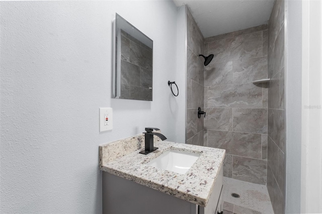 full bathroom featuring tiled shower and vanity