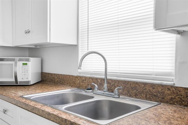 interior details with dark countertops, white cabinets, a sink, and white microwave