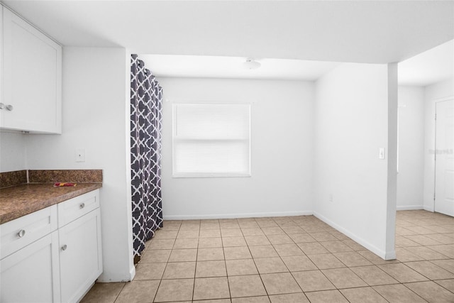 kitchen featuring light tile patterned floors, dark countertops, white cabinetry, and baseboards