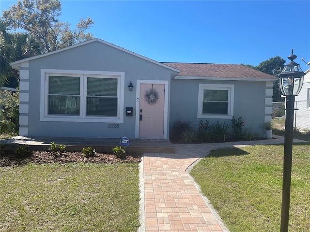 view of front of property with a shingled roof, a front yard, and stucco siding