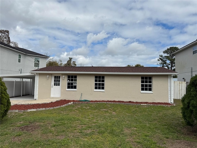 back of property with fence, an attached carport, a lawn, and stucco siding