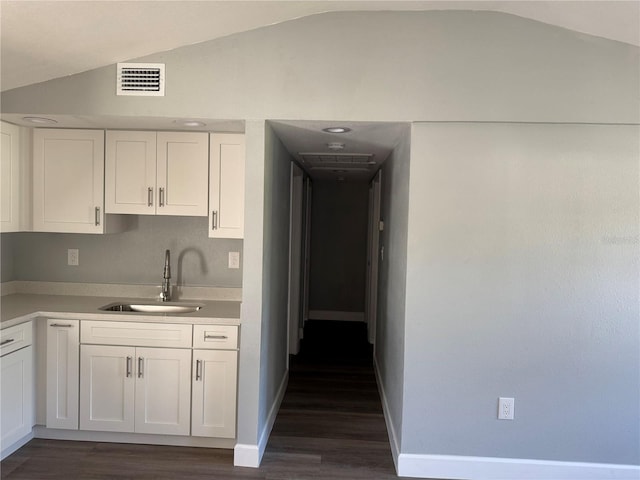 kitchen featuring visible vents, lofted ceiling, light countertops, white cabinetry, and a sink