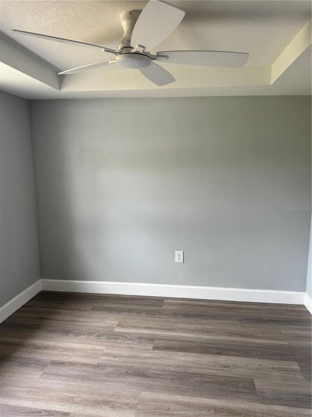 unfurnished room featuring a tray ceiling, ceiling fan, a textured ceiling, wood finished floors, and baseboards