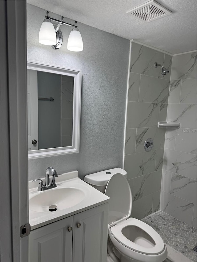 bathroom with a textured wall, toilet, vanity, visible vents, and a stall shower