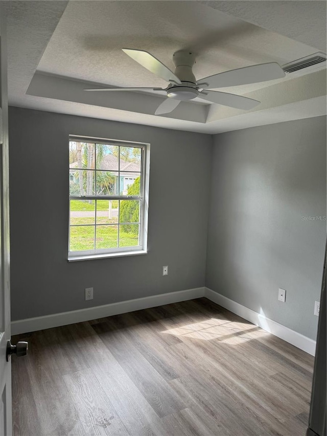 unfurnished room with baseboards, visible vents, a raised ceiling, and wood finished floors