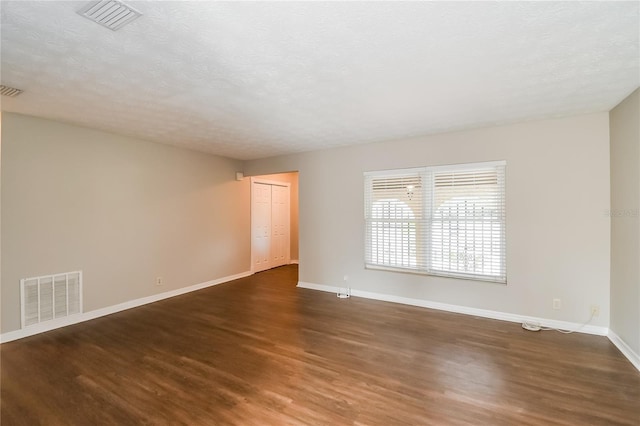 unfurnished room with a textured ceiling, wood finished floors, visible vents, and baseboards