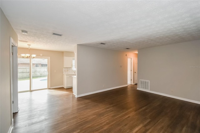 empty room with an inviting chandelier, visible vents, and dark wood-style flooring