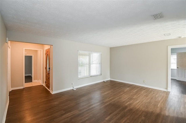 empty room with visible vents, a healthy amount of sunlight, and dark wood-type flooring