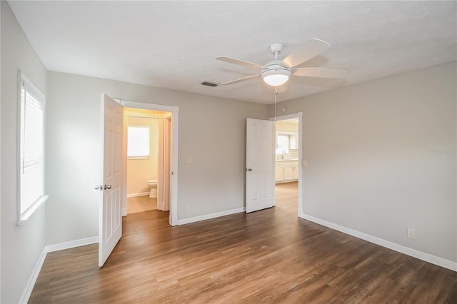 unfurnished bedroom with visible vents, multiple windows, baseboards, and wood finished floors