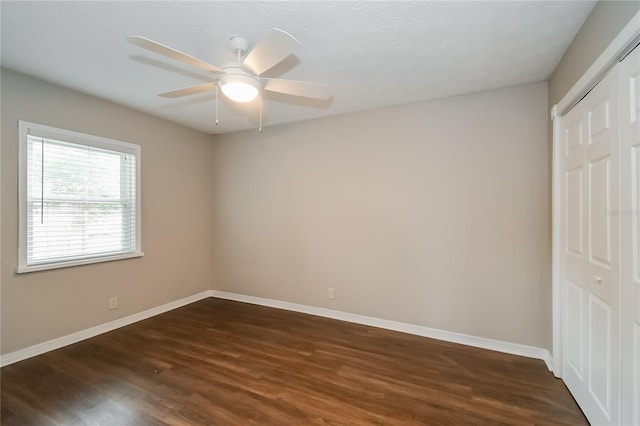 unfurnished bedroom with a closet, baseboards, dark wood-type flooring, and ceiling fan