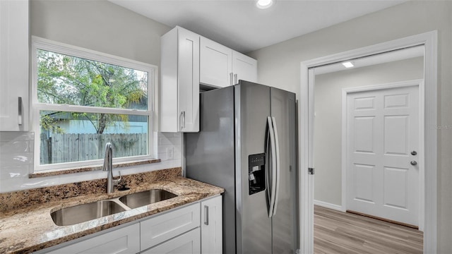 kitchen with light stone counters, a sink, white cabinetry, stainless steel refrigerator with ice dispenser, and backsplash