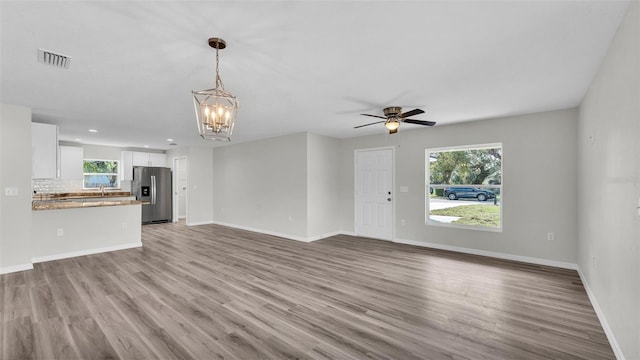 unfurnished living room with ceiling fan with notable chandelier, visible vents, baseboards, and wood finished floors