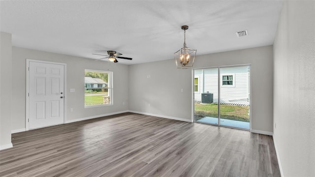 spare room with ceiling fan with notable chandelier, visible vents, baseboards, and wood finished floors