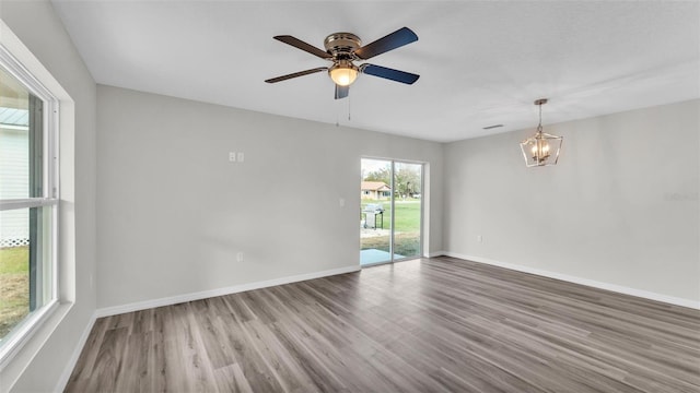 empty room with ceiling fan with notable chandelier, wood finished floors, visible vents, and baseboards