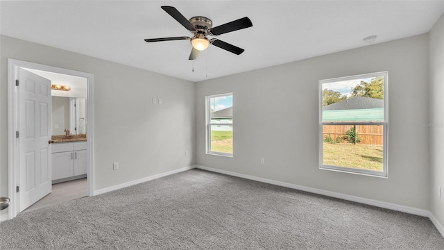 unfurnished bedroom with ensuite bath, baseboards, a ceiling fan, and light colored carpet