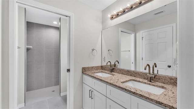 bathroom featuring visible vents, a sink, a tile shower, and double vanity