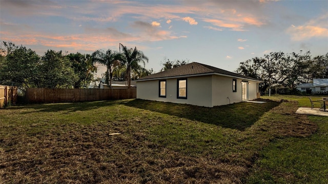 property exterior at dusk with a yard, fence, and stucco siding